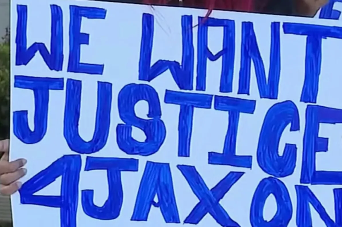 Transparent board with blue writing that says "WE WANT JUSTICE 4 JAXON"