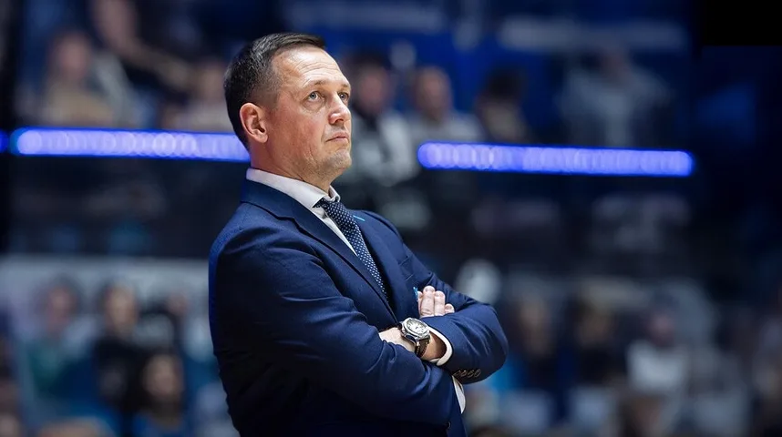 Muškarac u plavom odijelu i sa plavom kravatom sa tačkastim uzorkom, gleda u daljinu sa rukama prekrštenim na grudima.