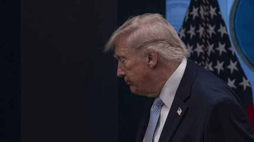 Donald Trump u tamnom odijelu i plavoj kravati sa američkom zastavom u pozadini