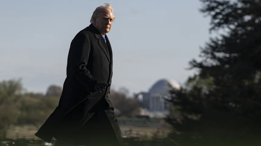 Donald Trump u crnom kaputu i rukavicama šeta ispred zgrade sa kupolom.