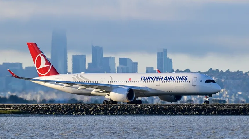 Avion Turkish Airlines na aerodromu sa gradom u pozadini.