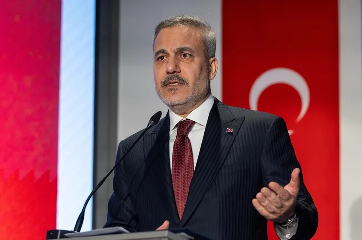 Portret turskog političara koji govori za govornicom, sa turskom zastavom u pozadini.