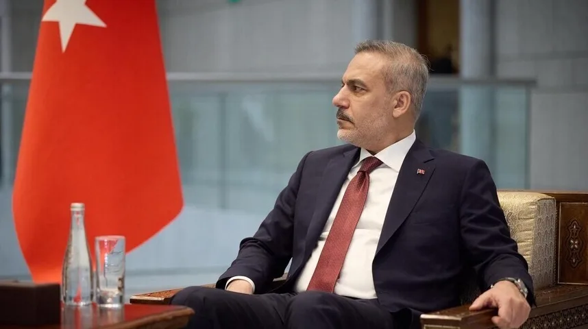 Turski političar u odijelu sjedi pored turske zastave.