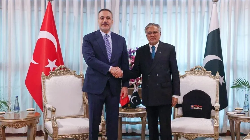 Dvije zastave, turska i pakistanska, nalaze se iza dva muškarca u odijelima koja se rukuju.