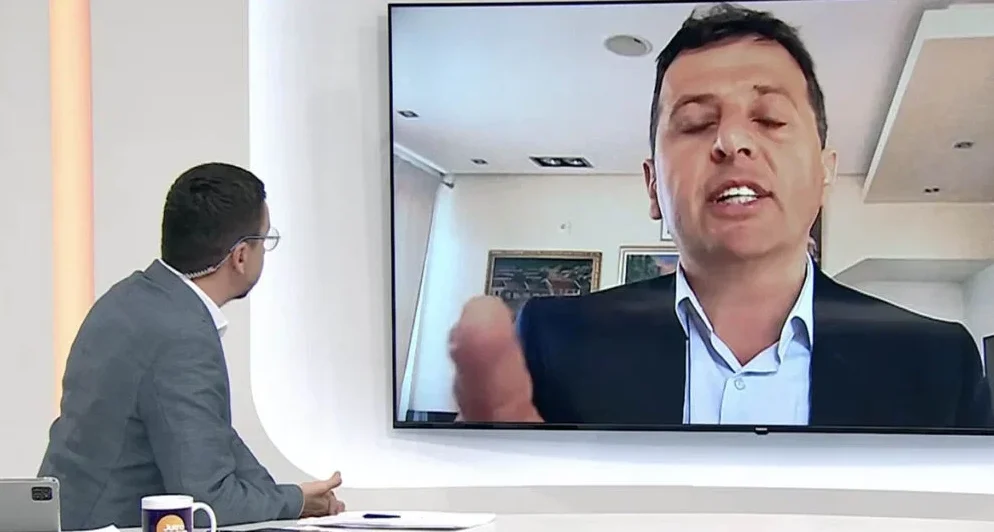 Muškarac u odijelu i bijeloj košulji gleda u ekran televizora gdje se prikazuje drugi muškarac