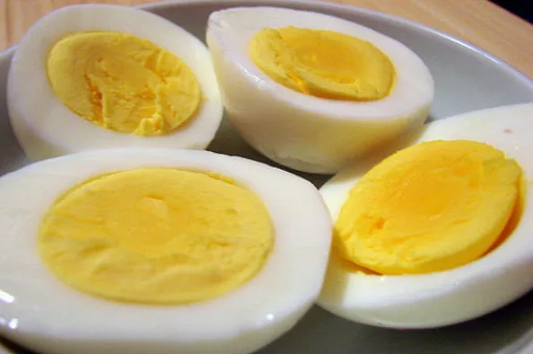 Četiri prepolovljena tvrdo kuhana jaja sa žutim žumancem, servirana u bijeloj posudi.