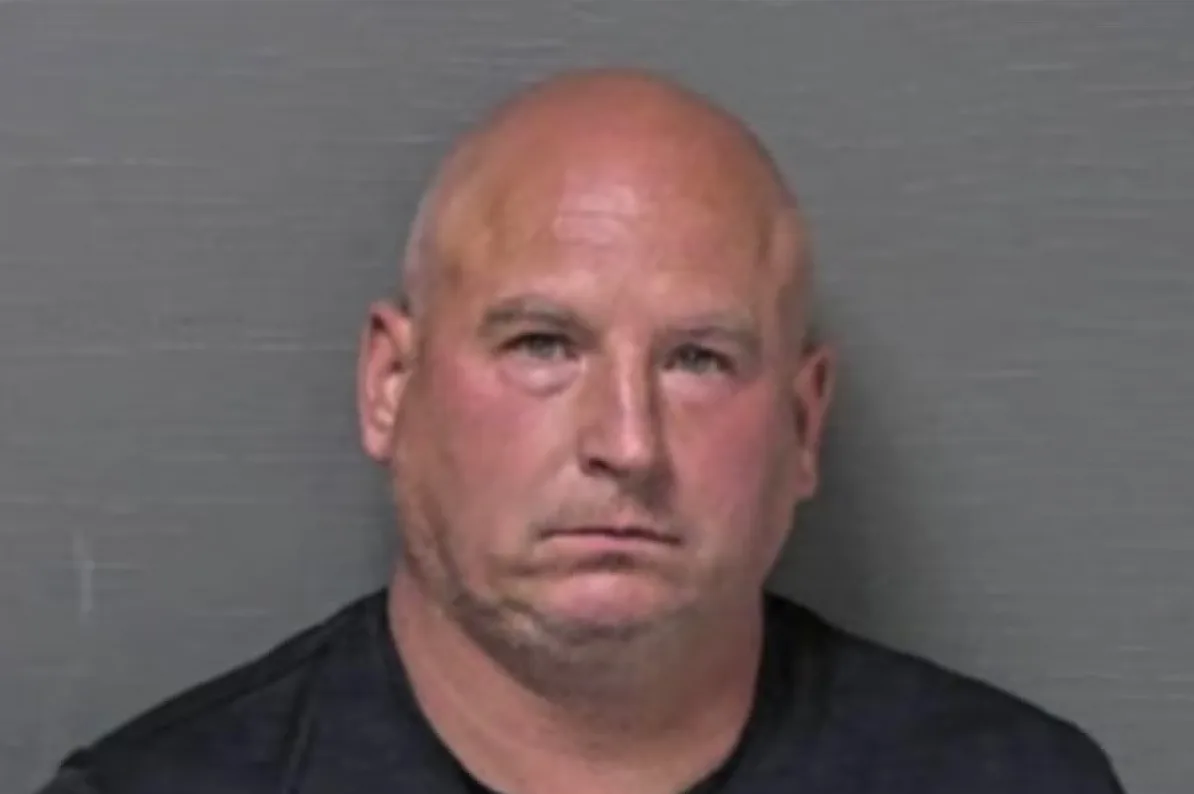 Fotografija uhapšenog muškarca sa ćelavom glavom i kratkom bradom, obučenog u crnu majicu, na tamnosivoj pozadini.