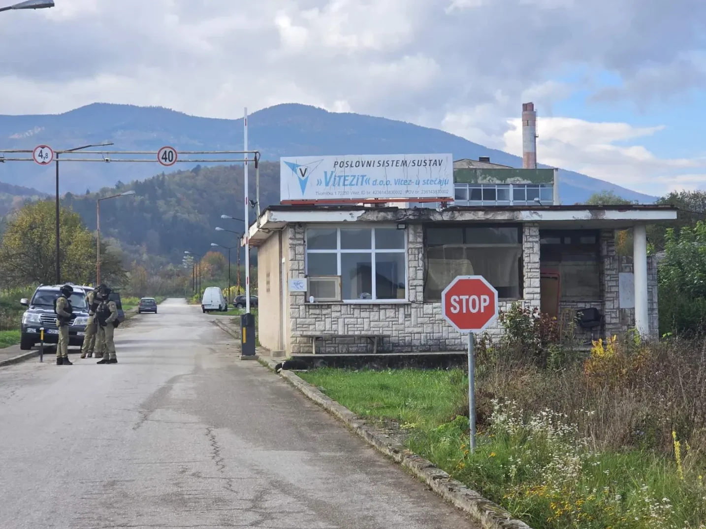 Sigurnosno osoblje u uniformama ispred ograde firme i zgrade sa znakom stop.