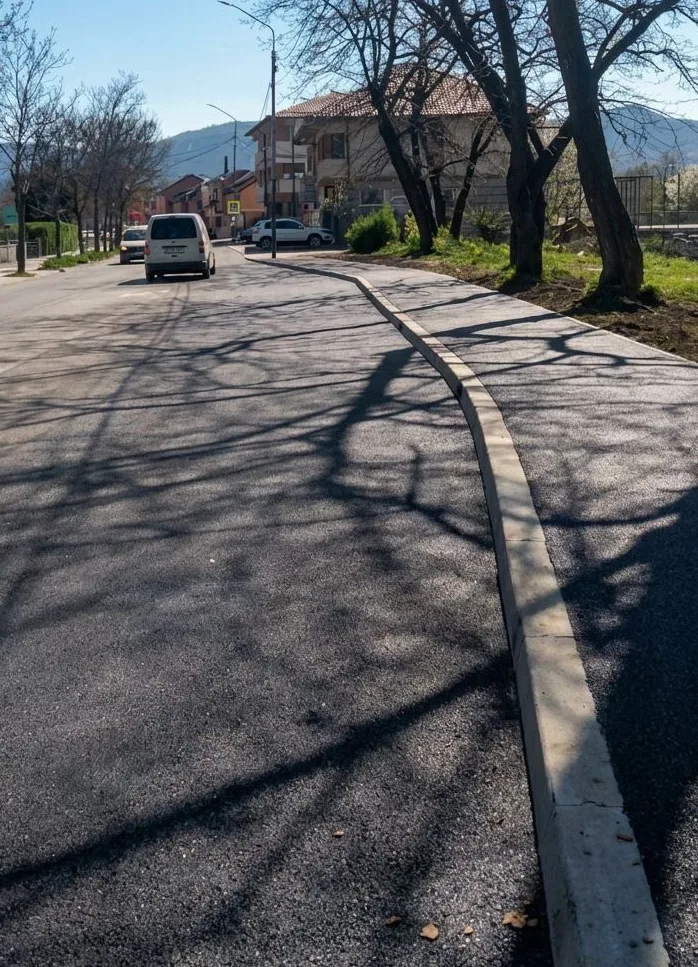 Novopoložen asfalt na gradskoj ulici sa biciklističkom stazom i betonskim ivičnjakom.