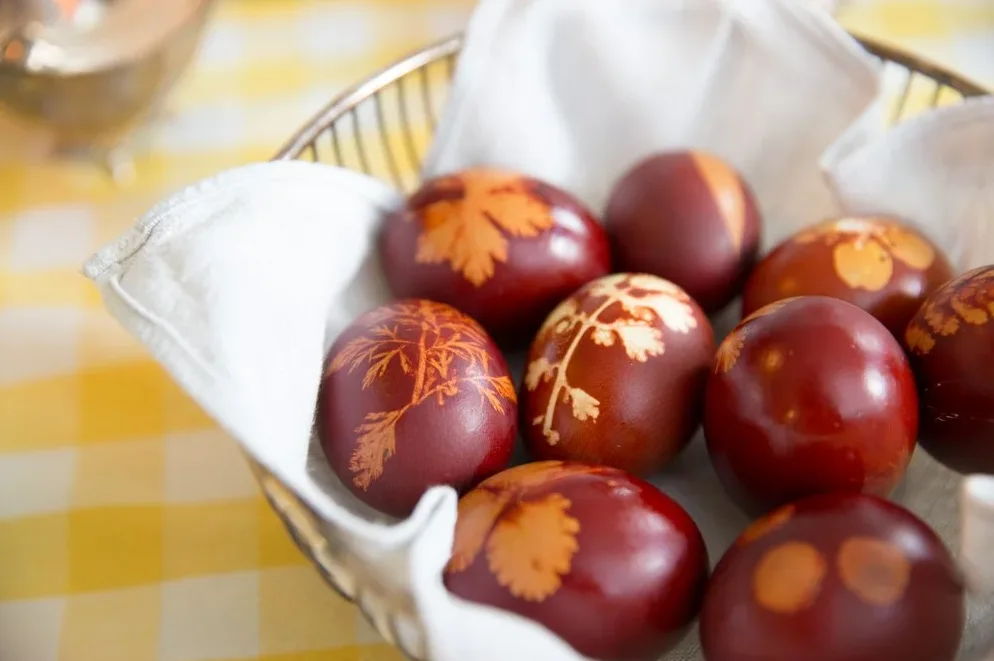Krupni kadar na tamno crvena uskršnja jaja ukrašena biljnim motivima, složena u metalnoj košarici obloženoj bijelim platnom.
