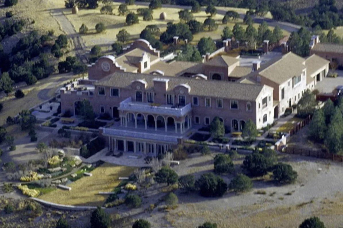 Vazdušni snimak velike, luksuzne vile sa crvenim krovom, terasama i baštom okružene zelenilom i brdovitim terenom.