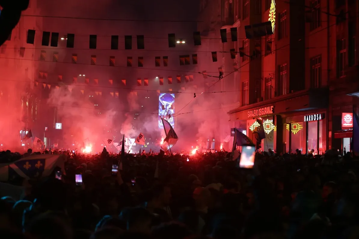 Skupina ljudi na ulici noću, osvijetljena crvenim dimom baklji i zastavama.