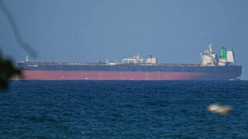 Ogroman teretni brod sa crvenim trupom i bijelom nadgradnjom plovi mirnim plavim morem pod vedrim nebom.