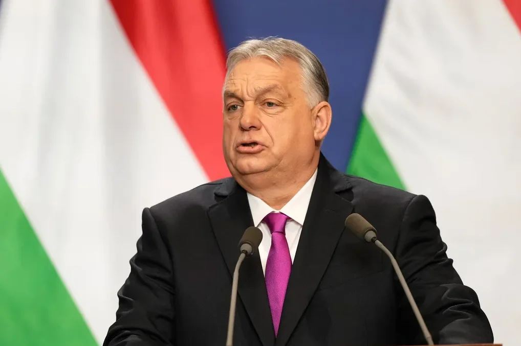 Viktor Orban sa roza kravatom govori za govornicu sa dva mikrofona, sa mađarskom zastavom u pozadini.