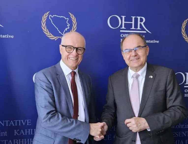 Visoki predstavnik i diplomat rukuju se ispred plave pozadine s logom OHR-a.