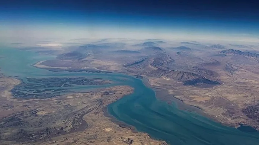 Vazdušni snimak rijeke koja protiče kroz suhi, planinski krajolik sa izrazitim naslagama sedimenta u blizini obale i plavim nebom u pozadini.