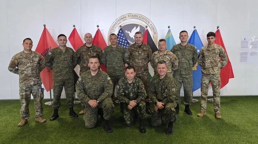 Grupa vojnih zvaničnika pozira ispred zastava više zemalja, uključujući Sjedinjene Američke Države, Albaniju i druge.