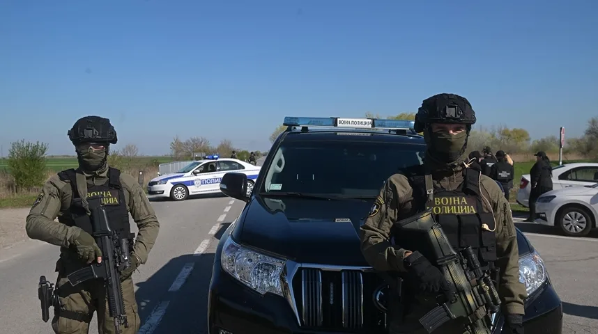 Dva pripadnika vojne policije u punoj opremi, naoružani, stoje pored službenih vozila.