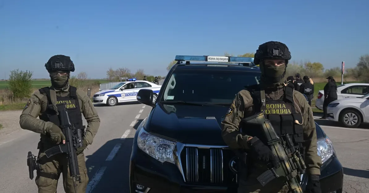 Dva pripadnika vojne policije s automatskim puškama ispred službenog vozila.