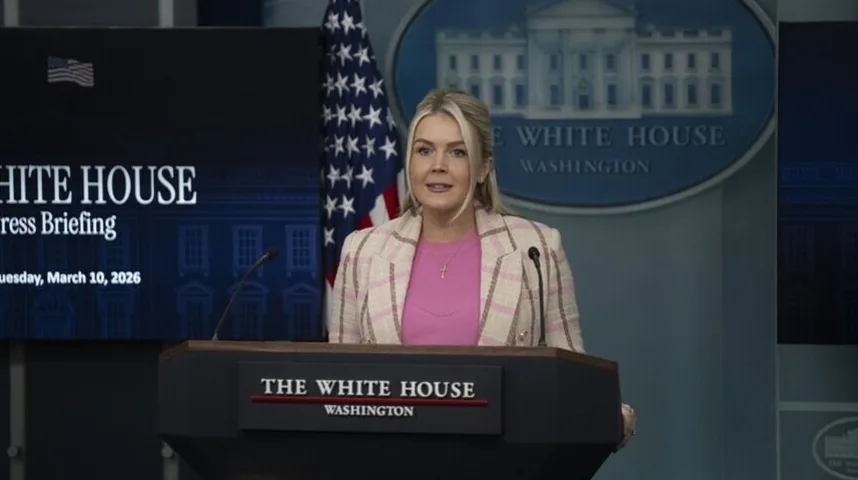 Žena sa plavom kosom u roze bluzi i kariranom sakou stoji za govornicom u Bijeloj kući.