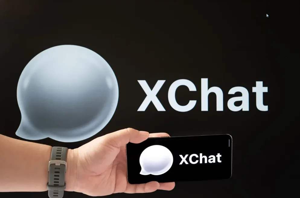 Logo XChat aplikacije prikazan na crnom ekranu telefona koji drži osoba sa pametnim satom