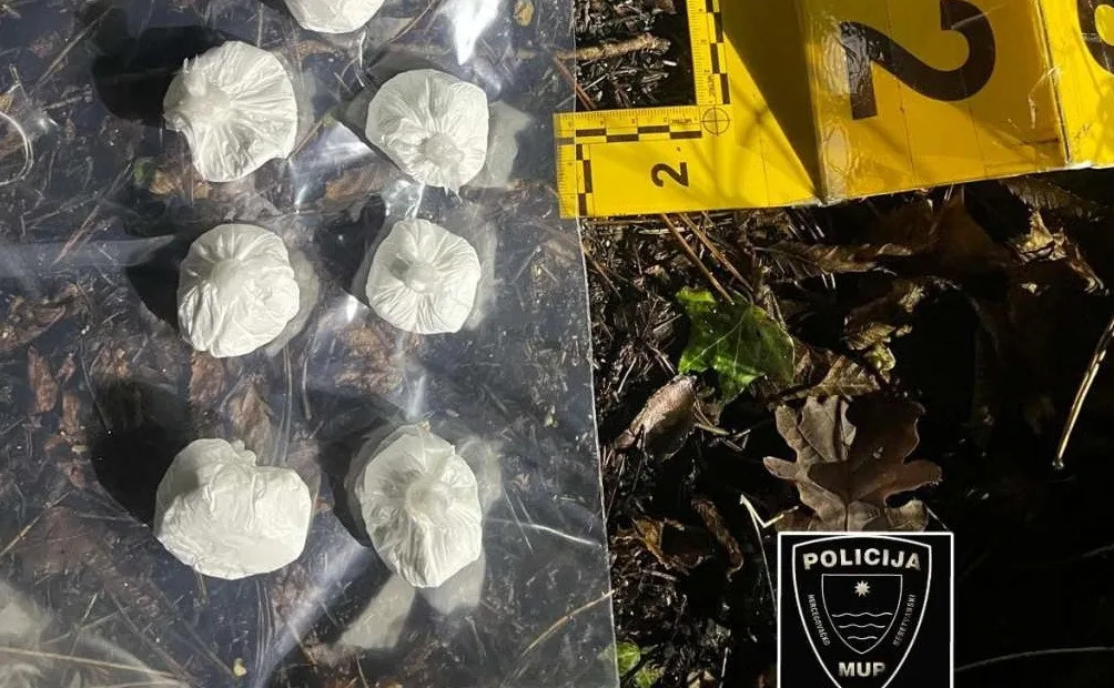 Policijska akcija zapljene droge, paketići bijele supstance u plastičnoj vrećici pored trake za obilježavanje mjesta događaja i policijskog grba.