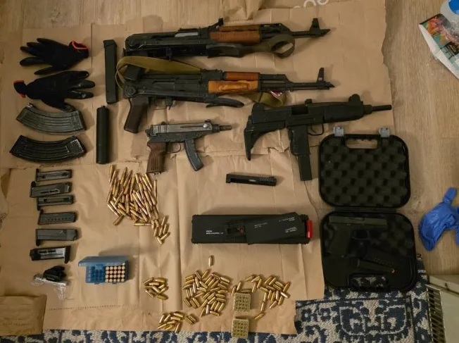 Krupni plan zaplijenjenog vatrenog oružja, uključujući automatske puške tipa AK-47, pištolj, ručni automatski pištolj, te veliku količinu municije i dodatnih dijelova.