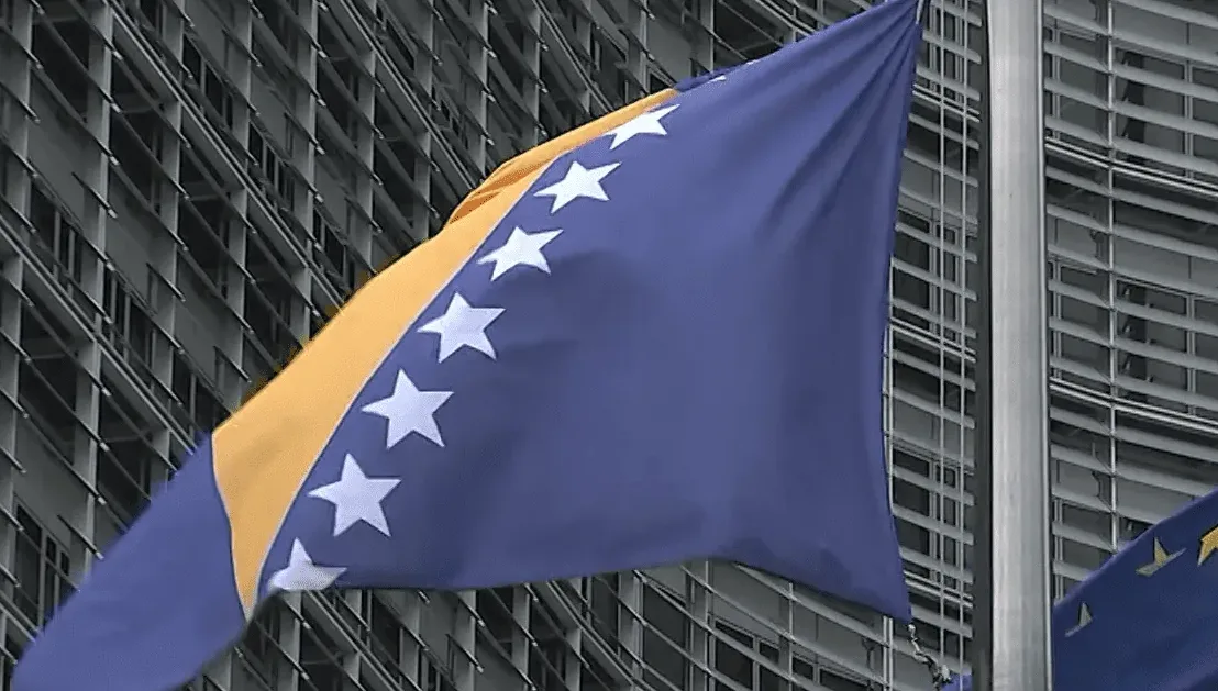 Zastava Bosne i Hercegovine koja leprša na vjetru ispred fasade moderne zgrade.