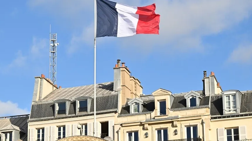 Francuska trobojnica leprša na vjetru iznad klasičnih pariških zgrada sa dimnjacima i potkrovnim prozorima.