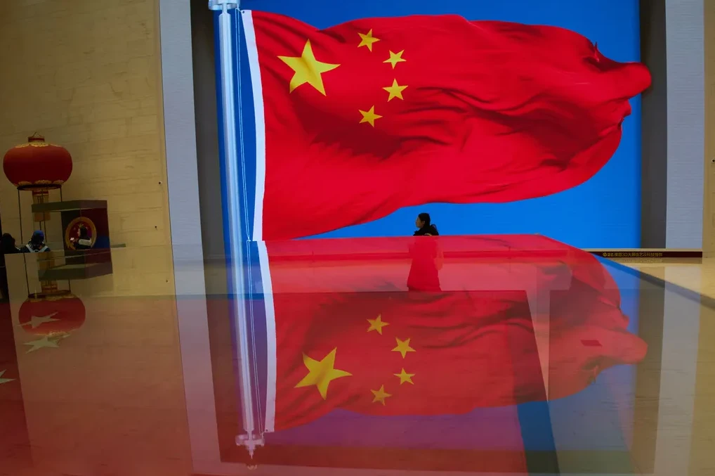 Crvena zastava Kine sa žutim zvijezdama, djelomično prekrivena odrazom