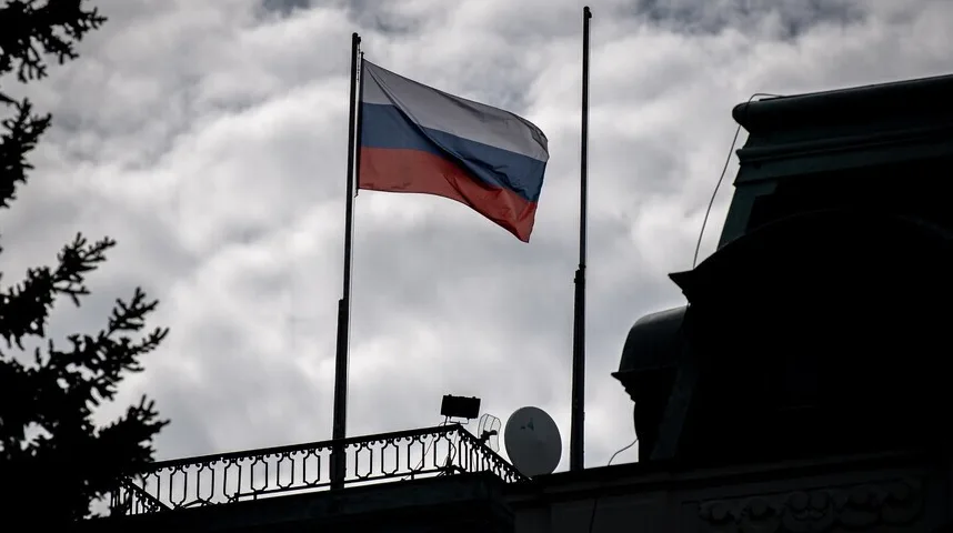 Silueta ruske zastave na jarbolu, ispred oblačnog neba, iznad dijela zgrade sa satelitskom antenom.