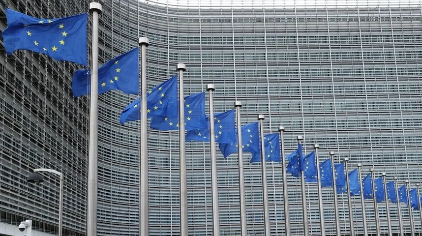 Zastave Evropske unije na jarbolima ispred moderne zgrade sa staklenom fasadom.