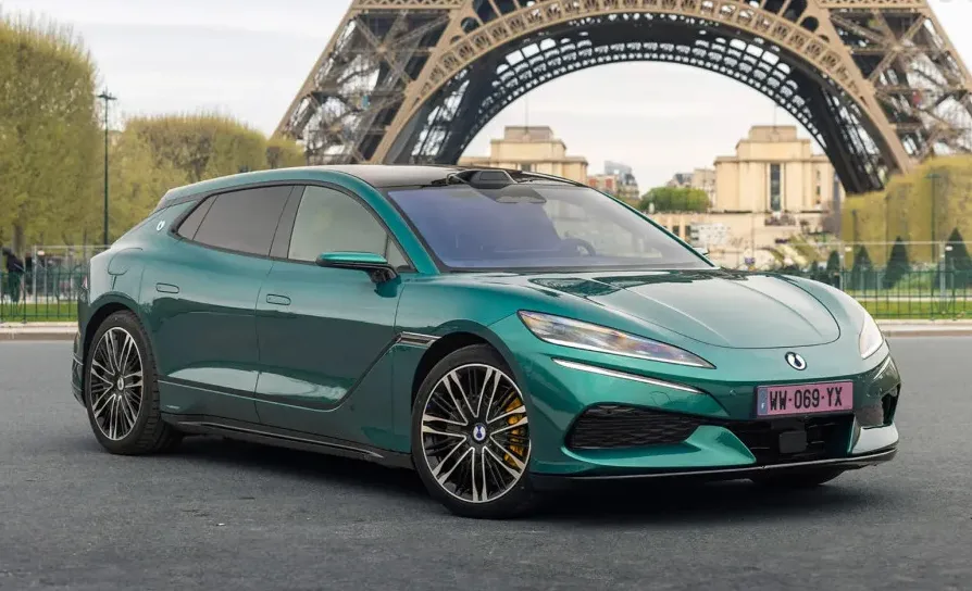 Moderni zeleni automobil marke ORA sa detaljima u crnoj boji, parkiran na ulici ispred Ajfelovog tornja u Parizu.