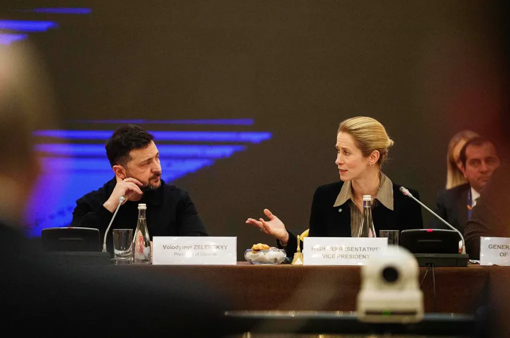 Volodimir Zelenski sjedi za stolom s predstavnicom, gledaju jedno drugo i razgovaraju.