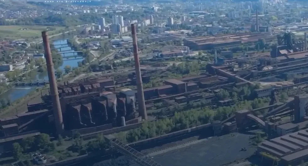 Panoramski pogled iz zraka na kompleks Željezare Zenica sa visokim dimnjacima i industrijskim postrojenjima.