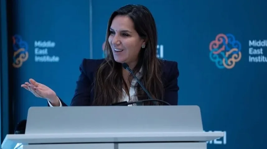 Žena u tamnom sakou i bijeloj košulji govori za govornicom, s podignutom desnom rukom. U pozadini je logo Middle East Institute.