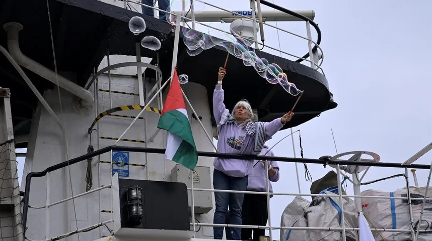 Žena pravi baloniće od sapunice na brodu, dok je pored nje istaknuta zastava Palestine.