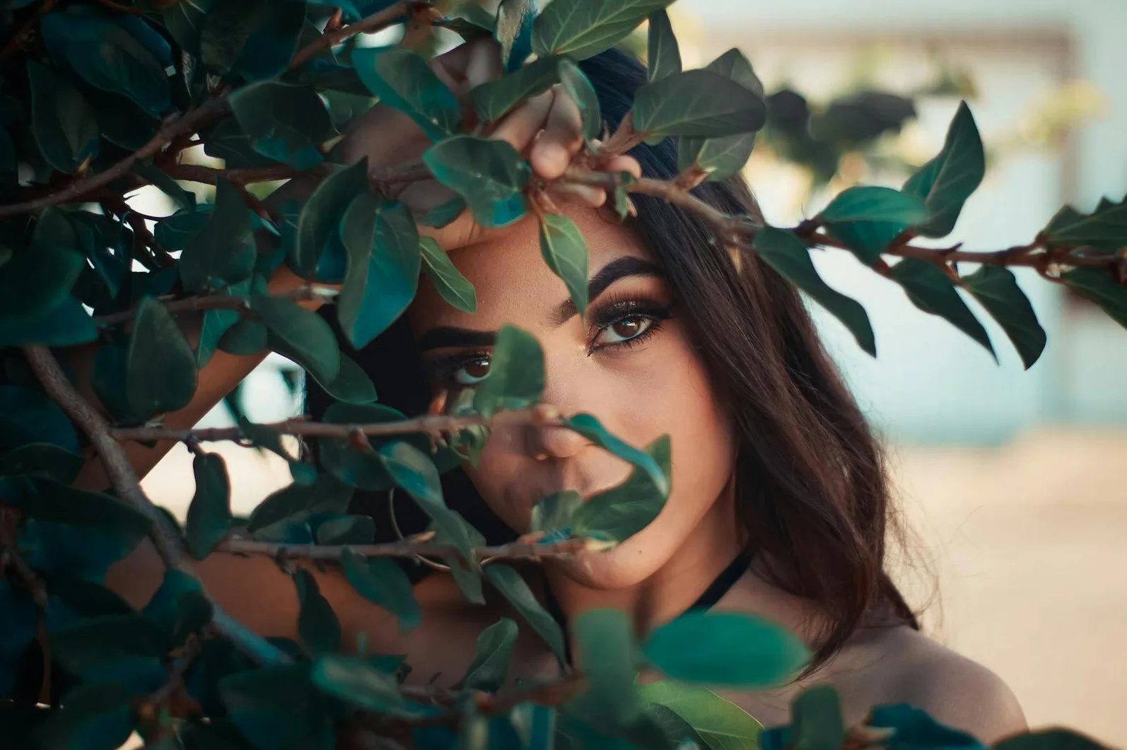 Bliski kadar mlade žene čiji je pogled djelomično skriven iza zelenog lišća grana