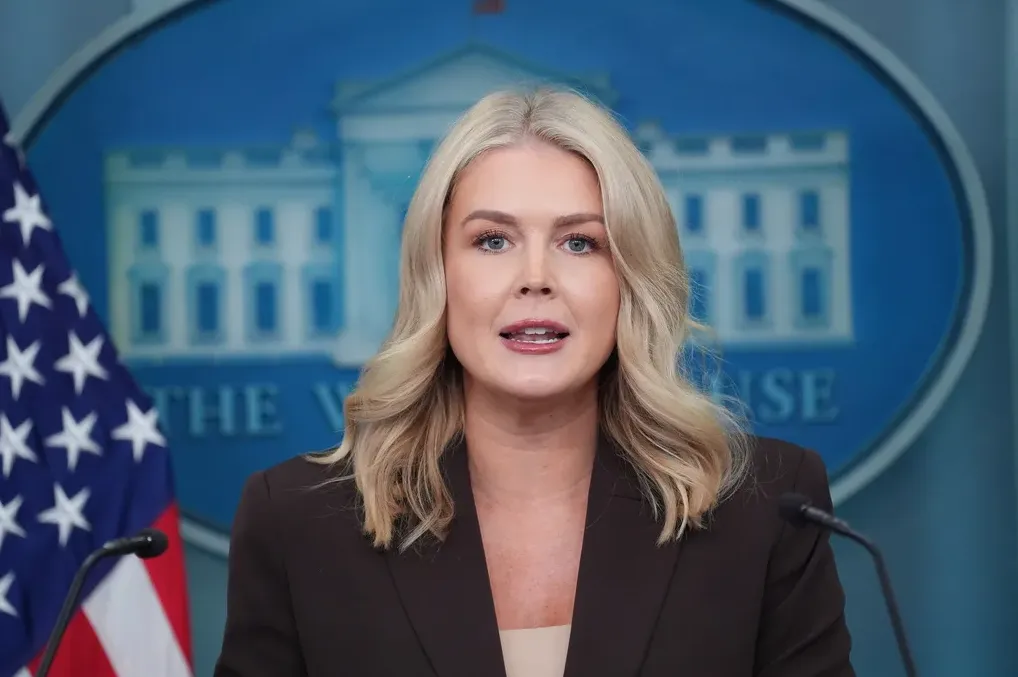 Plavokosa žena u tamnom sakou govori pred mikrofonom, sa zastavom SAD-a i logom Bijele kuće u pozadini.