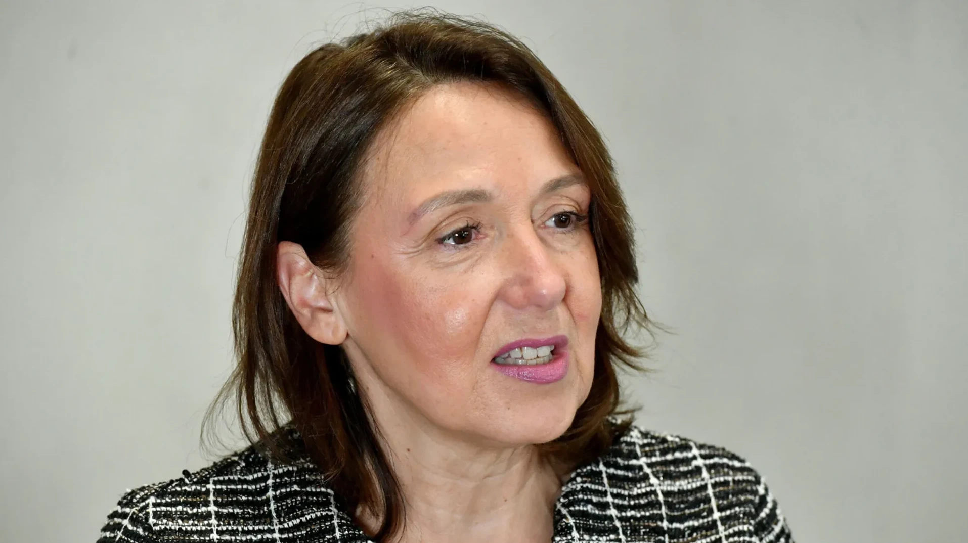 Portret žene sa smeđom kosom i ružičastim ružem na usnama, odjevena u crno-bijeli sako