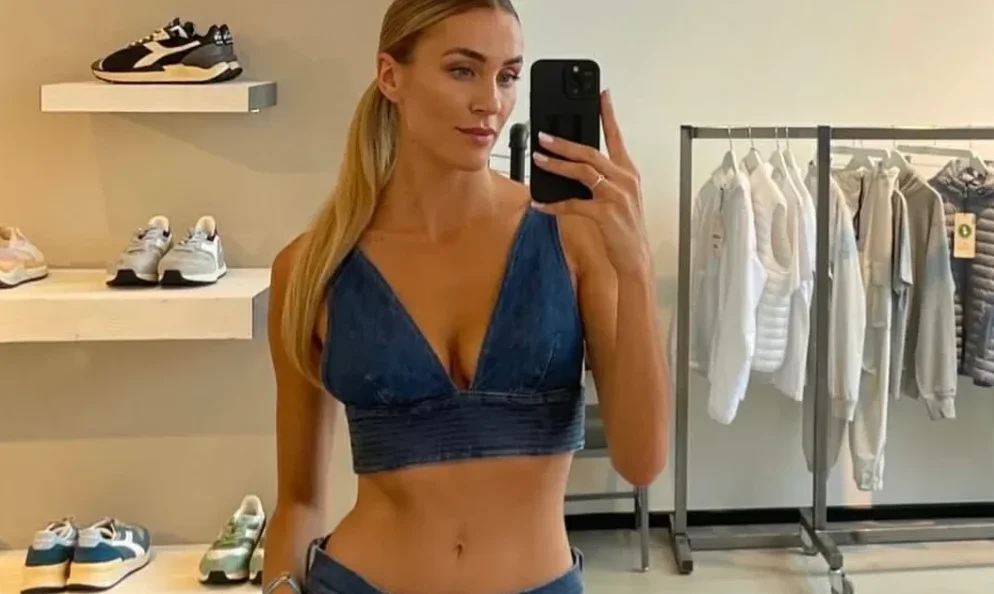 Žena nosi denim top i pantalone, pozirajući za selfi u prodavnici obuće i odjeće.