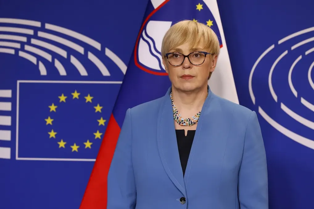 Potpredsjednica Evropske komisije Dubravka Šuica u plavom odijelu sa šarenom ogrlicom, stoji ispred zastave Evropske unije i zastave Slovenije.