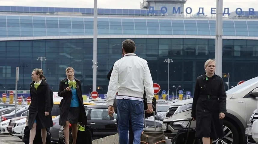 Muškarac s koferom i tri žene u crnim kaputima i zelenim maramama ispred aerodroma Domodedovo u Moskvi.