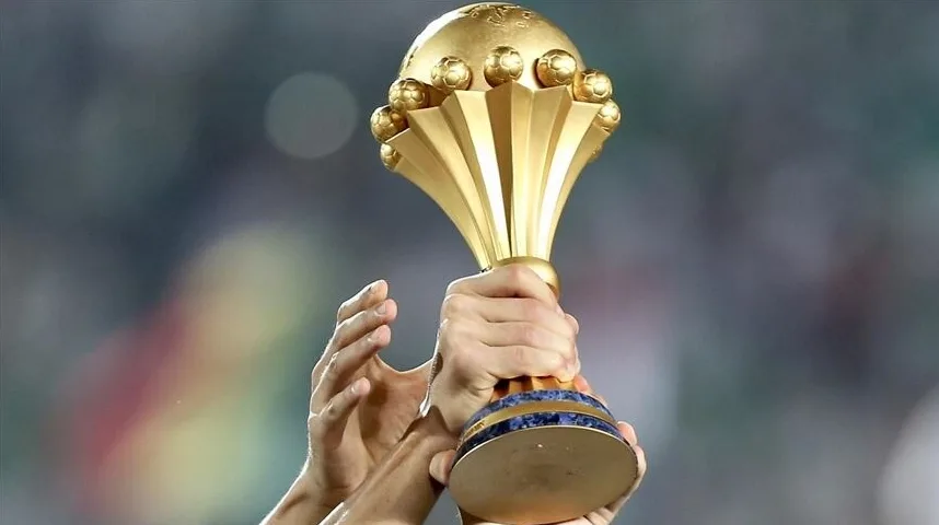 Ruke drže zlatni trofej sa fudbalskim loptama na vrhu