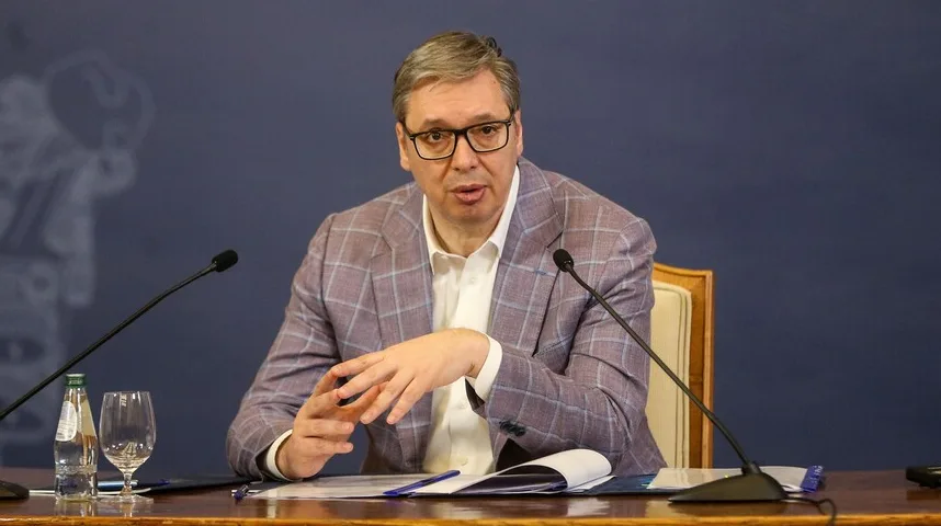 Aleksandar Vučić sjedi za stolom i govori, noseći karirani sako i naočale.