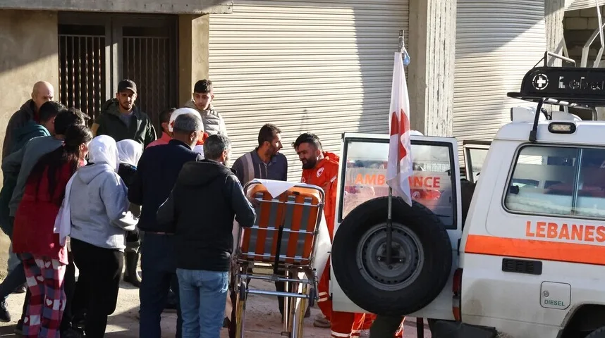 Ambulantna kola sa zastavom Crvenog krsta i grupa ljudi ispred zgrade.
