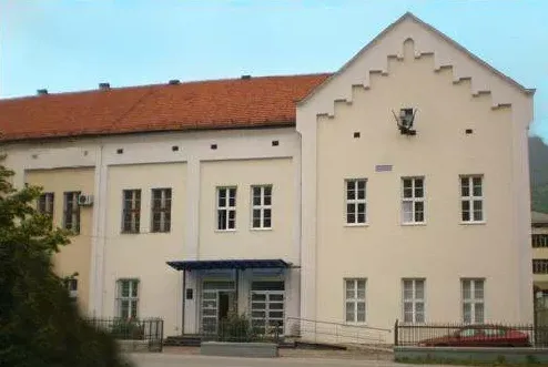 Fasada svijetložute zgrade sa smeđim krovom i bijelim prozorima.