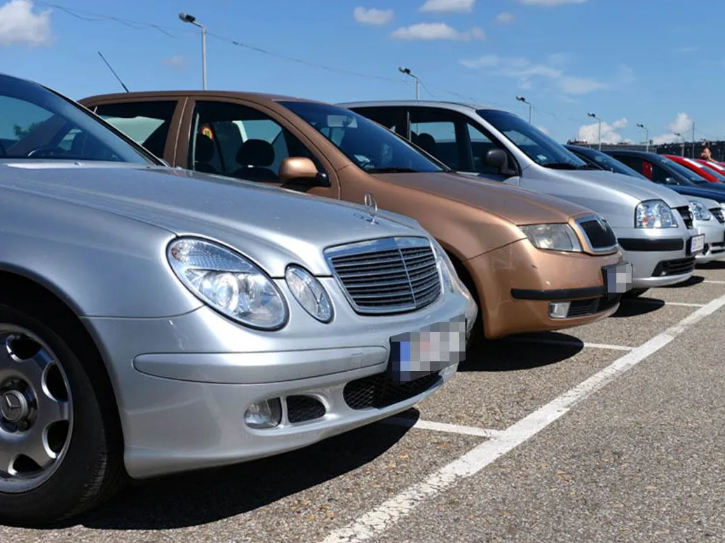 Red automobila različitih boja parkiranih na vanjskom parkingu pod vedrim nebom.