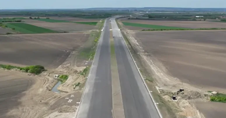 Aerialni snimak novog autoputa u izgradnji, koji prolazi kroz plodnu ravnicu sa obrađenim poljima.