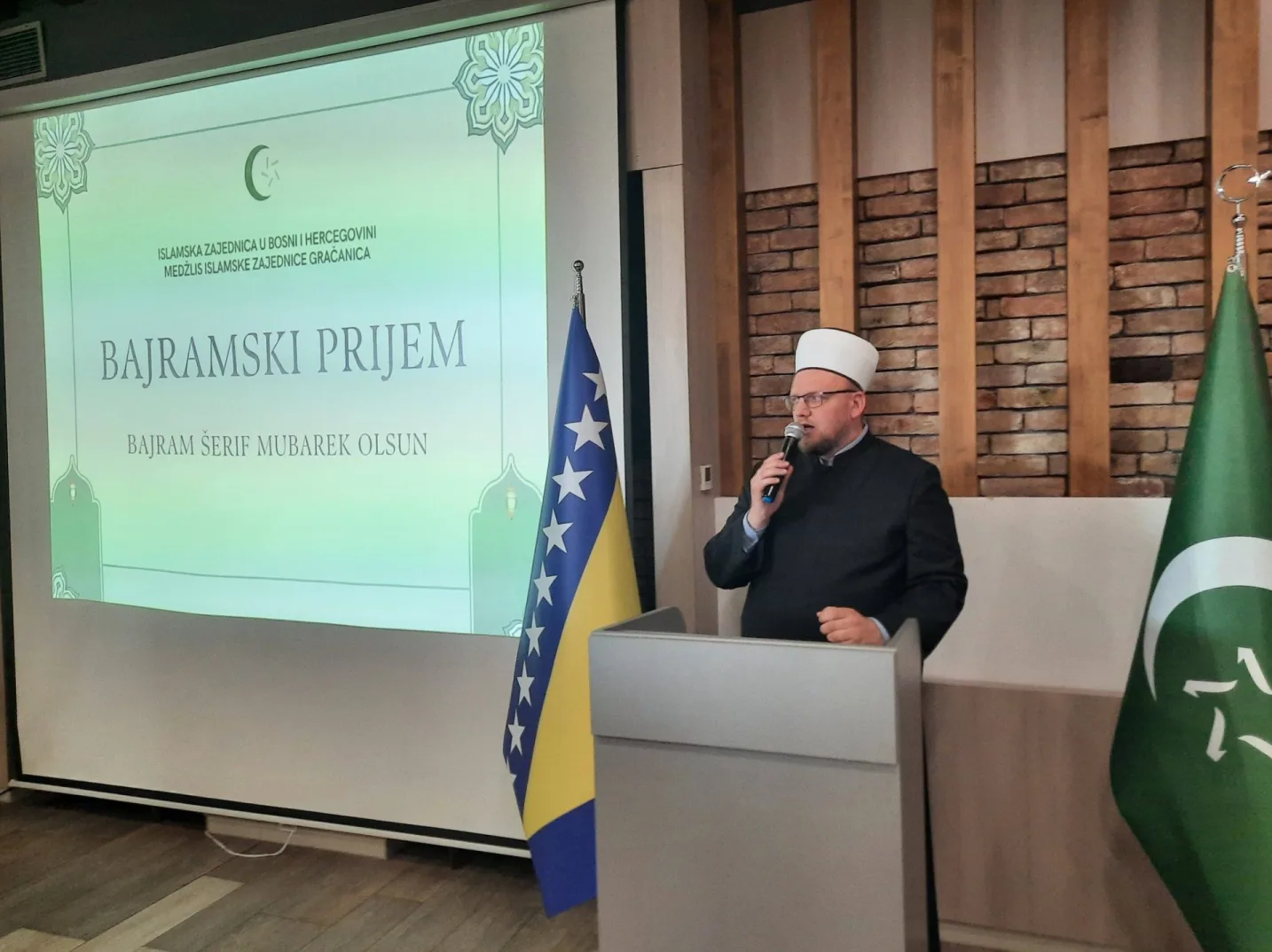 Imam u svečanoj odjeći drži govor pored zastave Bosne i Hercegovine na Bajramskom prijemu u Gračanici.
